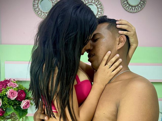 JonesAndJuly with long black hair, pink bra, and JonesAndJuly with short black hair, no shirt, kissing. JonesAndJuly's hand on JonesAndJuly's head, JonesAndJuly's hand on JonesAndJuly's neck.