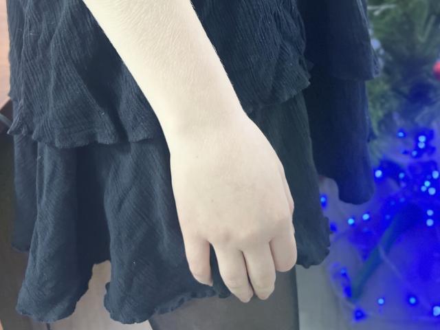 Laliina's pale hand with a slight pinkish tone, wearing a black, ruffled dress, is centered in the image. Her fingers are slightly curled, and she's standing.