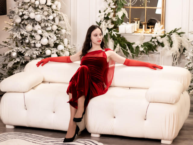StacieLove, vestido de veludo vermelho, luvas vermelhas, saltos pretos, sofá branco, batom vermelho, olhos vermelhos, cabelo preto ondulado, decoração de Natal, enfeites brancos e prateados, nádegas no sofá, braços abertos..