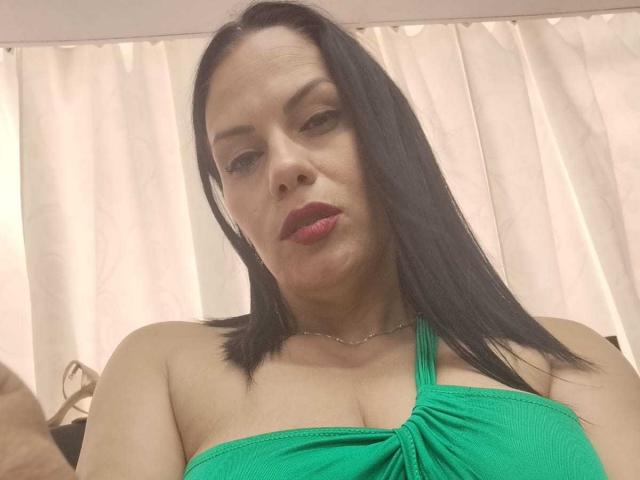 LizaRussell has medium tits, black straight hair, green halter top, red lipstick, light skin, and a neutral expression. She's wearing a thin necklace and looking slightly downward.