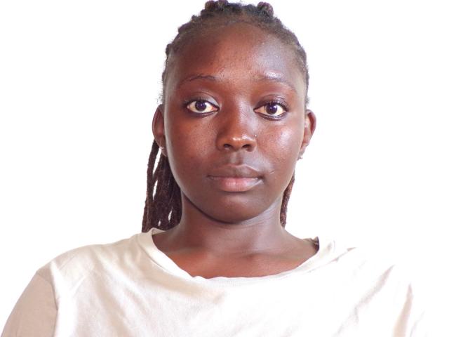 Lushmourine has dark brown skin, medium-sized shiny black eyes, and small brown nipples. She's wearing a white shirt with her braids falling to the sides.