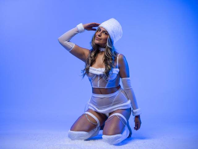 SunriseX knielend, gekleed in witte, doorschijnende lingerie met bontrand, een witte dijketting en een hoed, zwaait met haar rechterhand, blauwe achtergrond, lang blond haar, gemiddelde borsten, sexy..