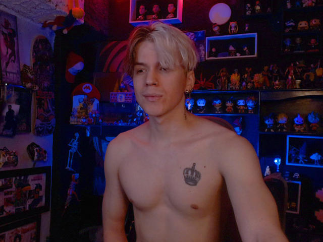 Shirtless RedTemptation with blonde hair, small crown tattoo on chest, smiling, blue neon lights, and a room full of toys and figurines in the background.