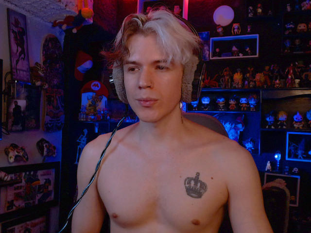 Shirtless RedTemptation with blonde and brown hair, wearing headphones, has a crown tattoo on his chest, and is looking at the camera with a slight smile.