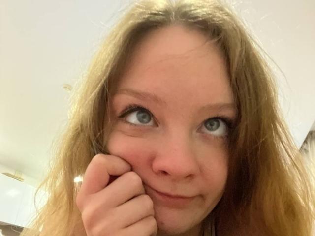 RadiantsLoves tiene una cara linda y sonriente, con ojos azules, cabello rubio ondulado y una mano tocándose la mejilla. Está mirando ligeramente hacia arriba con una expresión juguetona..