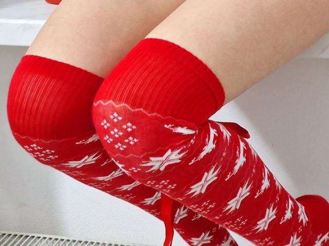Jumiera's red Christmas socks with white patterns are up to her knees. Her pale skin is visible. The socks are ribbed and have a festive design.