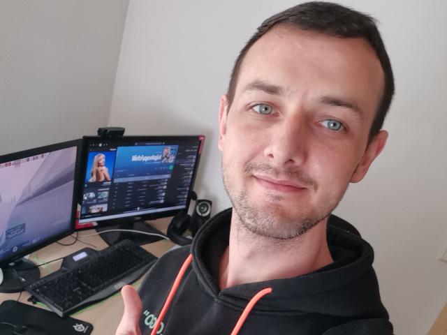 MichaelDawn, a cute dude with short brown hair, blue eyes, and a slight beard, wearing a black hoodie, smiling at the camera, thumbs up, in front of a computer.