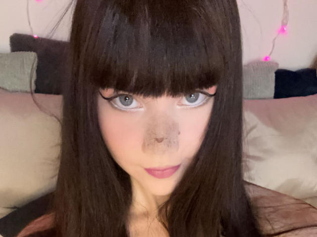 JennyMay ha i capelli castano scuro, gli occhi azzurri e un naso con piccole lentiggini. Guarda direttamente l'obiettivo con un leggero sorriso e rossetto rosa..