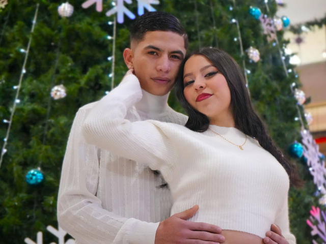 KylieAndJustin standing, KylieAndJustin's arm around Justin's neck, Justin's hand on KylieAndJustin's ass, Justin in white turtleneck, KylieAndJustin in white sweater, Christmas tree in background.