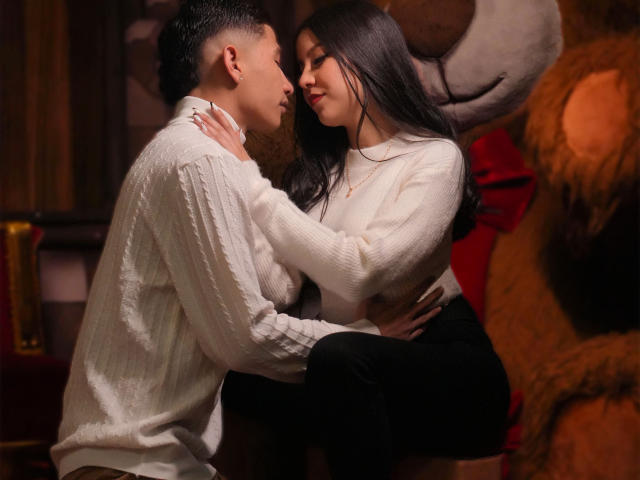 KylieAndJustin, with long black hair and white sweater, sits on Justin's lap. Justin, in a white knit shirt, holds her waist, eyes closed, in a sensual, intimate moment.