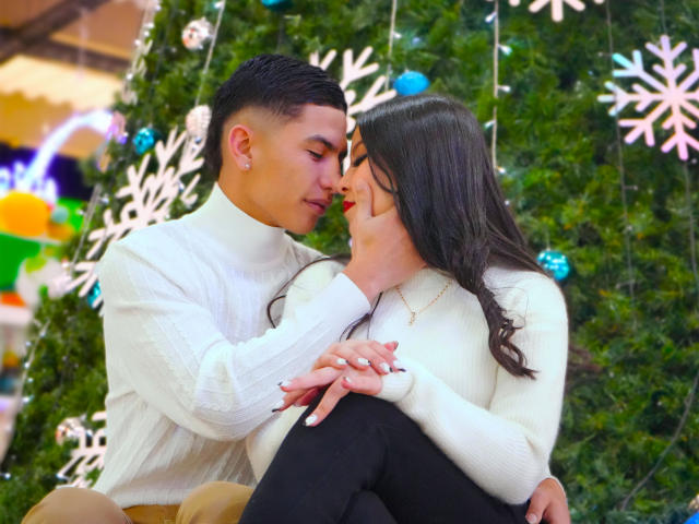 KylieAndJustin, a cute couple, are kissing with eyes closed. KylieAndJustin are wearing white turtlenecks, she has long black hair, he has short black hair, and they're holding hands.