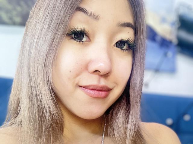 RenyLime has light brown skin, long straight blonde hair, green eyes with long black lashes, and a small beauty mark near her right eye. She's smiling with pink lips.