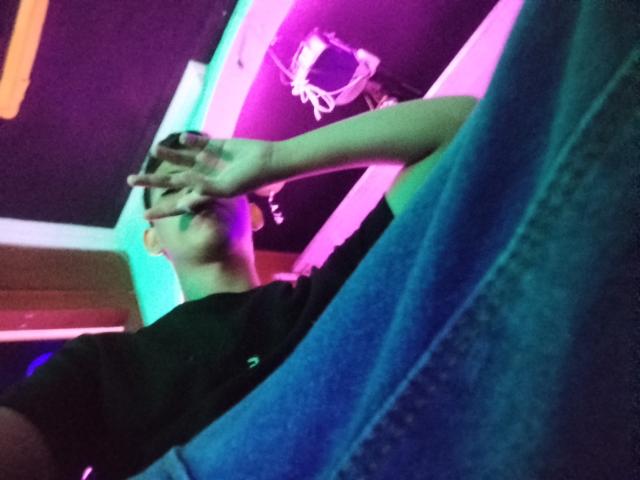 SexyAladinX covering his eyes with one hand, wearing a black shirt and blue jeans, under pink and purple neon lights with a basketball hoop in the background.