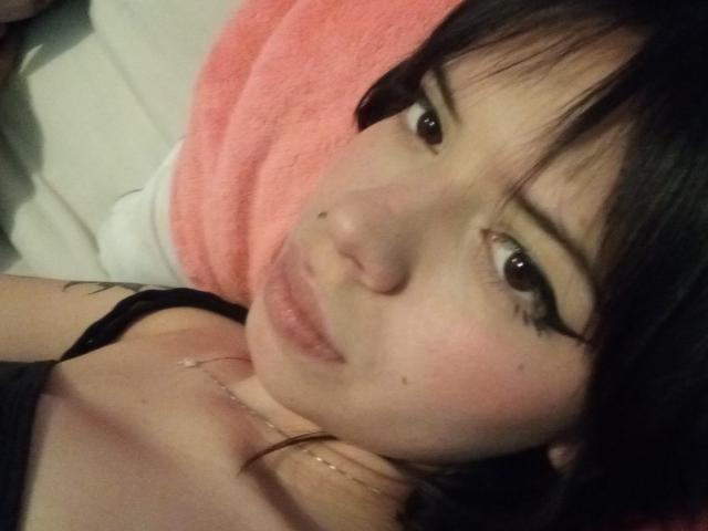 NatashaHottson's face with black eyeliner, pale skin, brown eyes, and a small beauty mark on her upper lip, lying on a pink towel, wearing a black top.