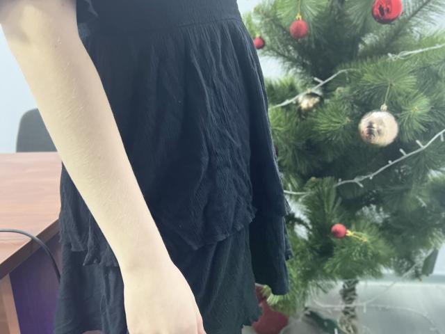 Laliina's pale arm in a black, textured dress stands beside a decorated Christmas tree with red and gold ornaments. Her arm's curve is visible, showing subtle skin texture.