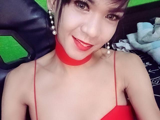 WifeMaterial with cute face, red lipstick, and red choker, wearing a red spaghetti top, smiling at the camera, pearl earrings, and short dark hair. Boobs visible, small, cute.