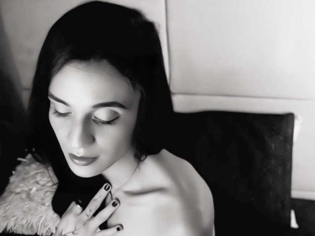 PamelaKander with dark hair, closed eyes, and black nail polish, has her hand on her bare chest, looking down with a subtle smile. Black and white photo.