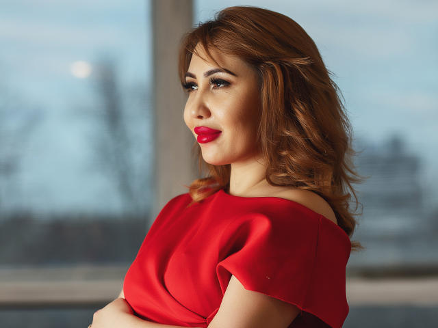 LiliNi with red lipstick, wavy brown hair, and a red off-shoulder dress, arms crossed, looking over shoulder, sexy, attractive, confident, soft light, clear skin.
