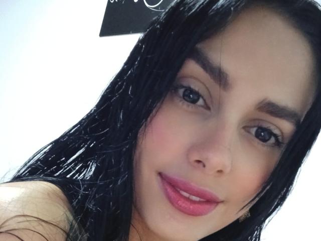 AnaisHilton has wet black hair, pink lips, and dark eyebrows, with blue eyes and a subtle smile, showing a cute and sexy face. Her tits are not visible.