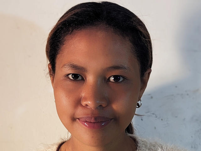KalliseHott has dark brown skin, shiny lips, small earrings, and straight black hair. Her face is centered, smiling slightly, with brown eyes looking directly at the camera.