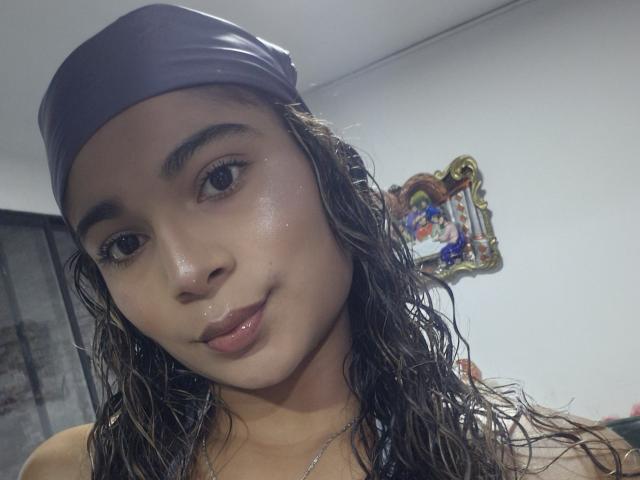 HottSunnyLove69 with wet brown hair, wearing a purple headscarf, glossy pink lips, and a slight smile, showing smooth, shiny skin and brown eyes in a selfie.