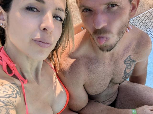 Annic, con grandes senos, lleva un top de bikini naranja, y un hombre con el pecho peludo y un tatuaje en el pectoral derecho, saca la lengua. Están junto a una piscina..
