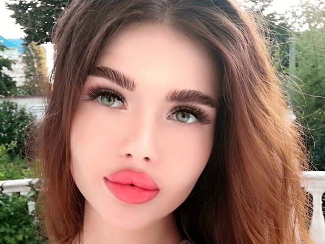 KatrinaBonita-hot with long brown hair, green eyes, thick eyebrows, long eyelashes, and bright pink lips, looking slightly to the side with a subtle smile.