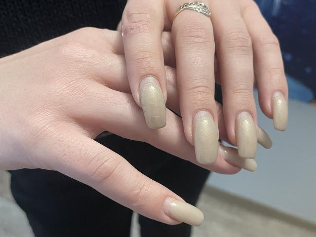 Vailett's hands with shiny, beige, almond-shaped nails, wearing a silver ring with small diamonds on her right ring finger, showing off her well-manicured, glossy nails.
