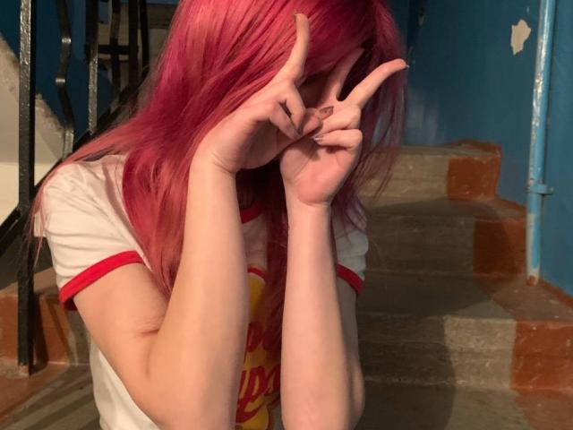 Lialit with pink hair, covering eyes with hands making a peace sign, wearing a white shirt with red trim, standing on a staircase, looking cute and shy.