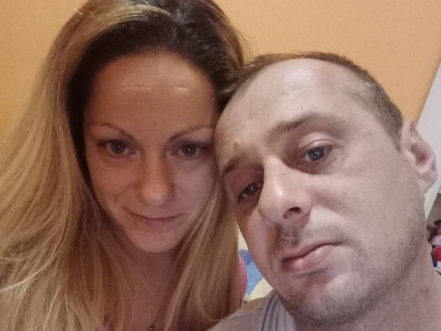 VickyMike, avec de longs cheveux blonds et de petites seins, est assise à côté d'un homme chauve au visage hirsute et au regard pensif, sur une photo de profil..