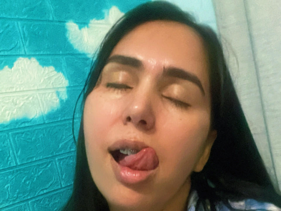 Aniliz, les yeux fermés, la langue tirée et la bouche légèrement ouverte, a la peau moite et les cheveux foncés, et a l'air séduisante. Ses petites fesses sont visibles dans la partie inférieure..