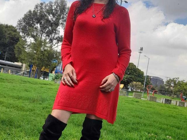 ArianaSanz in a red dress with long sleeves, black knee-high boots, and a necklace, standing on green grass, showing her ass and hands with rings.