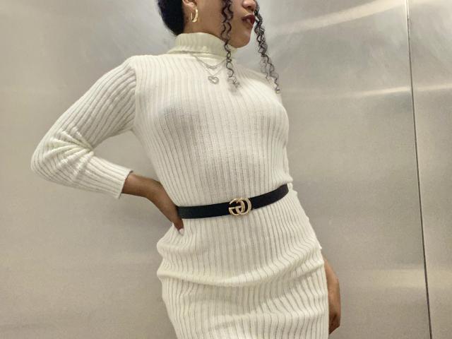 SophieSonyas wearing a white, ribbed, turtleneck dress with a black belt and gold Gucci logo, hands on hips, curly black hair, standing side profile, showing her ass.