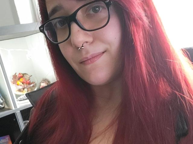 LadyJosefine-hot with red hair, black glasses, nose ring, and subtle smile, showing off her cute face and small, slightly upturned nose. Boobs not visible, focus on face.