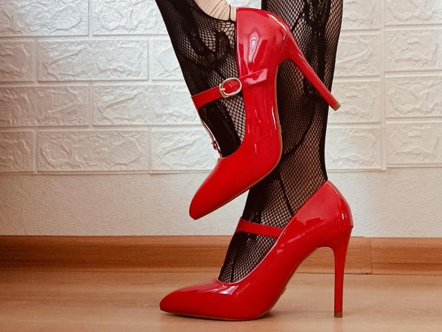 MartaLor's glanzende rode hoge hakken met een gouden gesp, staan op een houten vloer, ze draagt zwarte netpanty's, en laat haar sexy benen en puntige stiletto's zien..