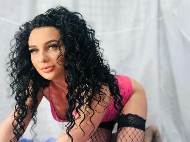 SweetSerena-hot with curly black hair, pink lace lingerie, and black fishnet stockings, on all fours, showing her tits and ass, with a sexy, confident expression.