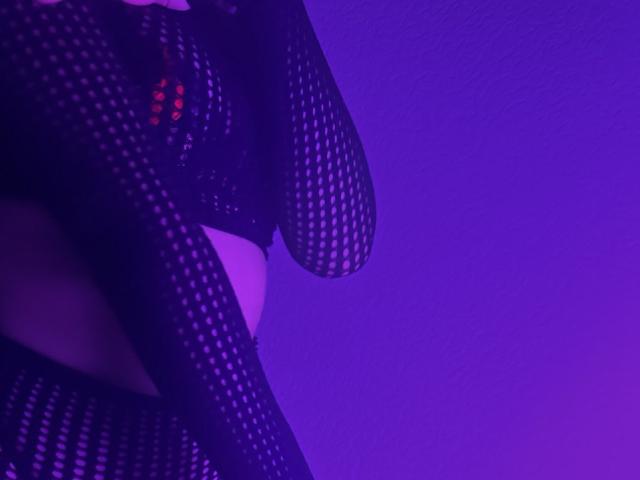 BalletSwan in black fishnet lingerie, showing a curve of her ass and a glimpse of her pussy, with purple lighting. Image focuses on her lower body.