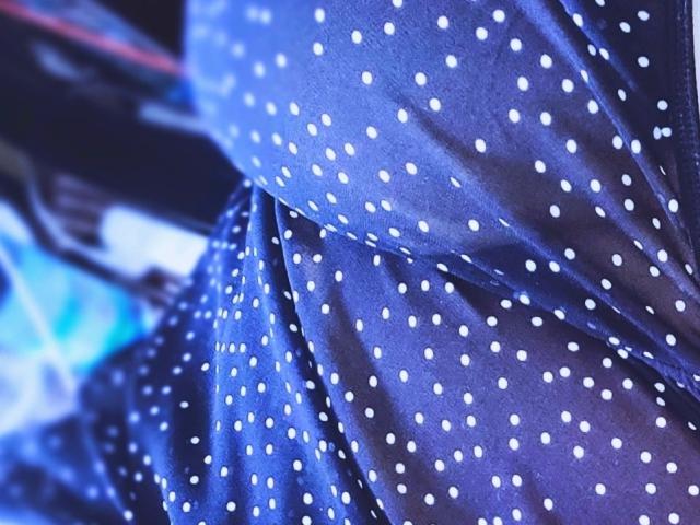 Das blaue, gepunktete Kleid von RinaBella, mit weißen Punkten, fällt über ihren Po und zeigt die Textur und das Muster des Stoffes. Der Fokus liegt auf dem oberen Teil des Kleides..