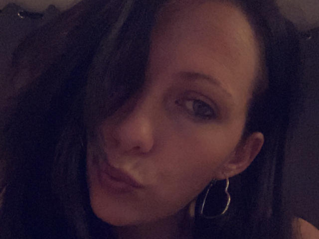 SamXFrenchie has dark hair, a heart-shaped earring, and a pouty face with a slightly shiny nose, lying down in dim lighting. Her eyes are partially visible.