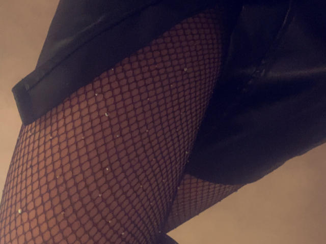 SamXFrenchie's legs in black fishnet stockings with small glittery dots, showing a partial view of their black skirt. Focus on the upper thigh and lower leg area.