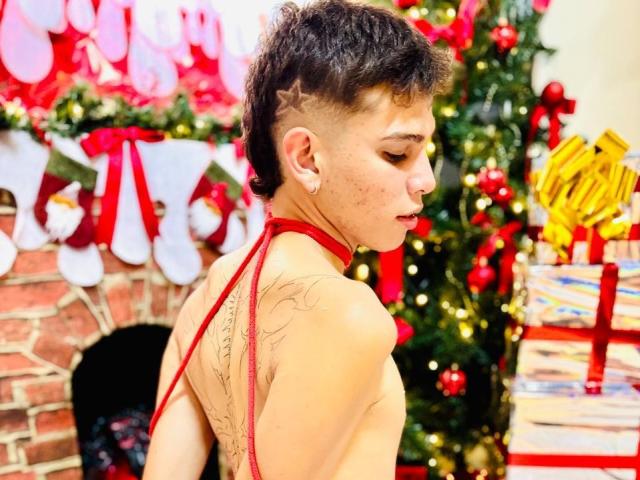 JassonSmith with short, dark hair, star tattoo on side, red halter top, visible back tattoo, small earrings, looking down, Christmas tree and presents in background, sexy, cute.