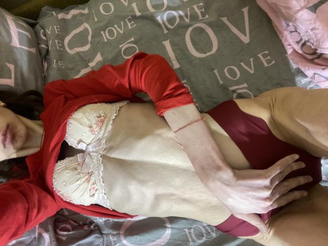 Kabblasha lying on bed, red shirt open, white lace bra, showing flat stomach, red panties, hand on hip, visible ass, pale skin, brown hair, red bracelet, partially cropped face.