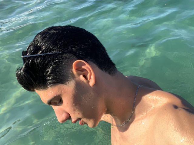 FabrizzioHot has wet black hair, a slight tan, and a silver necklace. His shiny, wet, bare shoulders are visible in clear, green water. His face is turned downward.