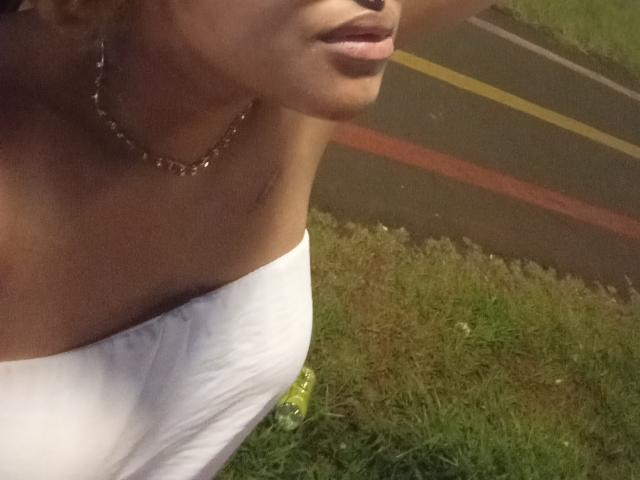 AmmyStar's face and upper chest, showing her pouty lips and bare shoulders with a white strapless top, wearing a chain necklace, with a grassy road in the background.
