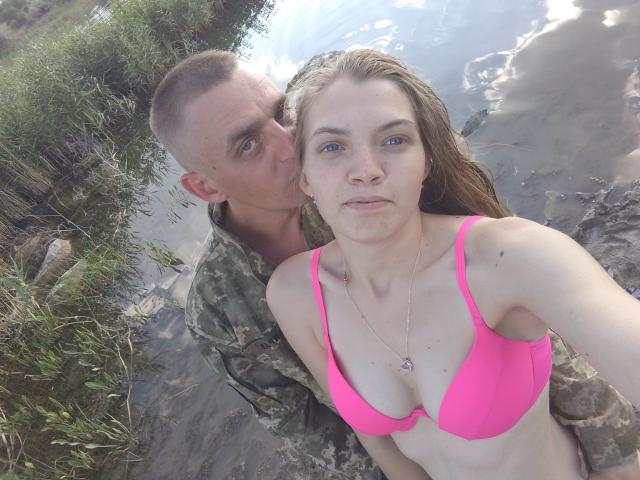 Een foto van ParaFox met kort bruin haar in camouflage, die de nek kust van ParaFox met blauwe ogen, een roze beha en nat bruin haar, terwijl ze in ondiep water staan..