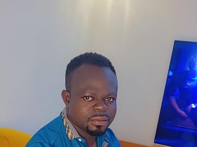 BoidBand, dark-skinned dude with short curly hair, blue shirt, gold chain, and goatee, sitting with a yellow couch, TV showing a blue screen on the right.