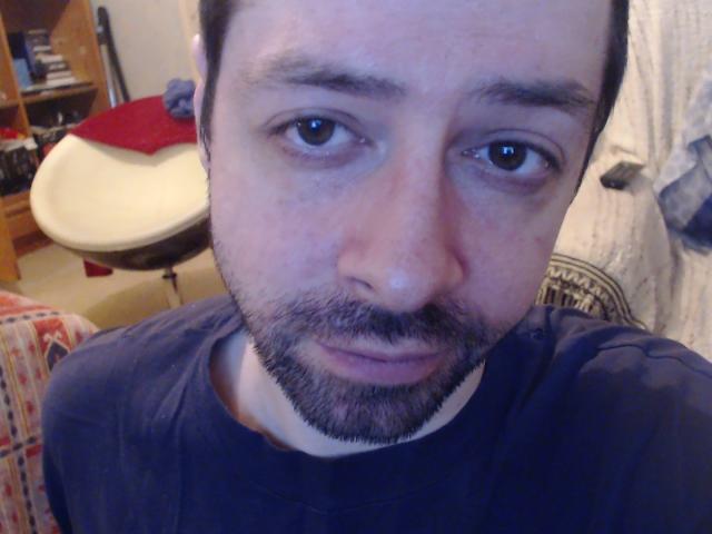 Klimov has a chubby face, short dark hair, and a beard. He's wearing a blue shirt, looking slightly bored with brown eyes. His nose is a bit red.