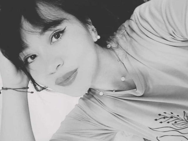 CharlotteBliss with short black hair, eyeliner, and lipstick, lying down, wearing a shirt with a leaf design, necklace, and bracelet, looking at the camera. Black and white photo.