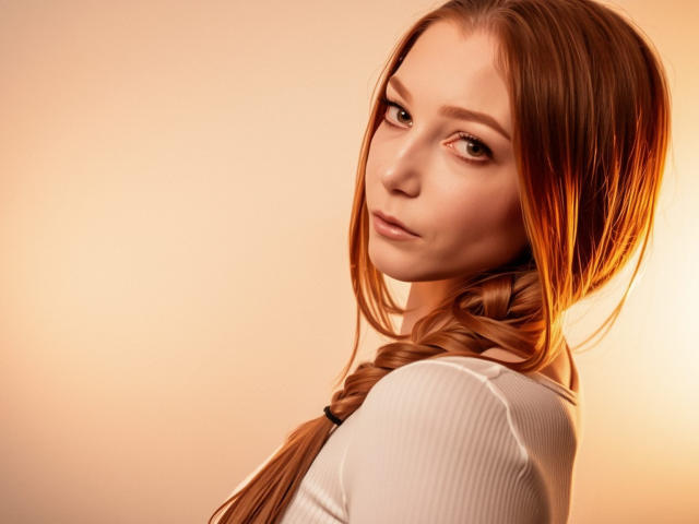 LovelyxEmilly with long red hair in a braid, wearing a white ribbed shirt, looking over her shoulder with a slight smile, soft warm lighting, subtle makeup.