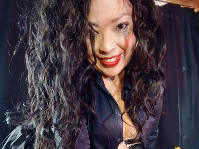 KarenCurlyHair with long, curly black hair, wearing a dark blue button-up shirt, smiling with red lipstick, winking, and showing a cute, sexy face, in a photo.
